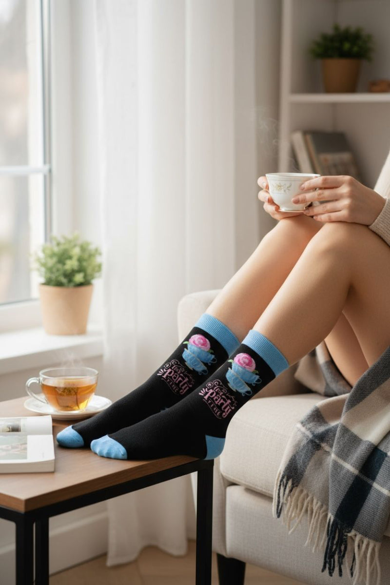 Person sitting on a couch wearing socks with floral designs, holding a cup.
